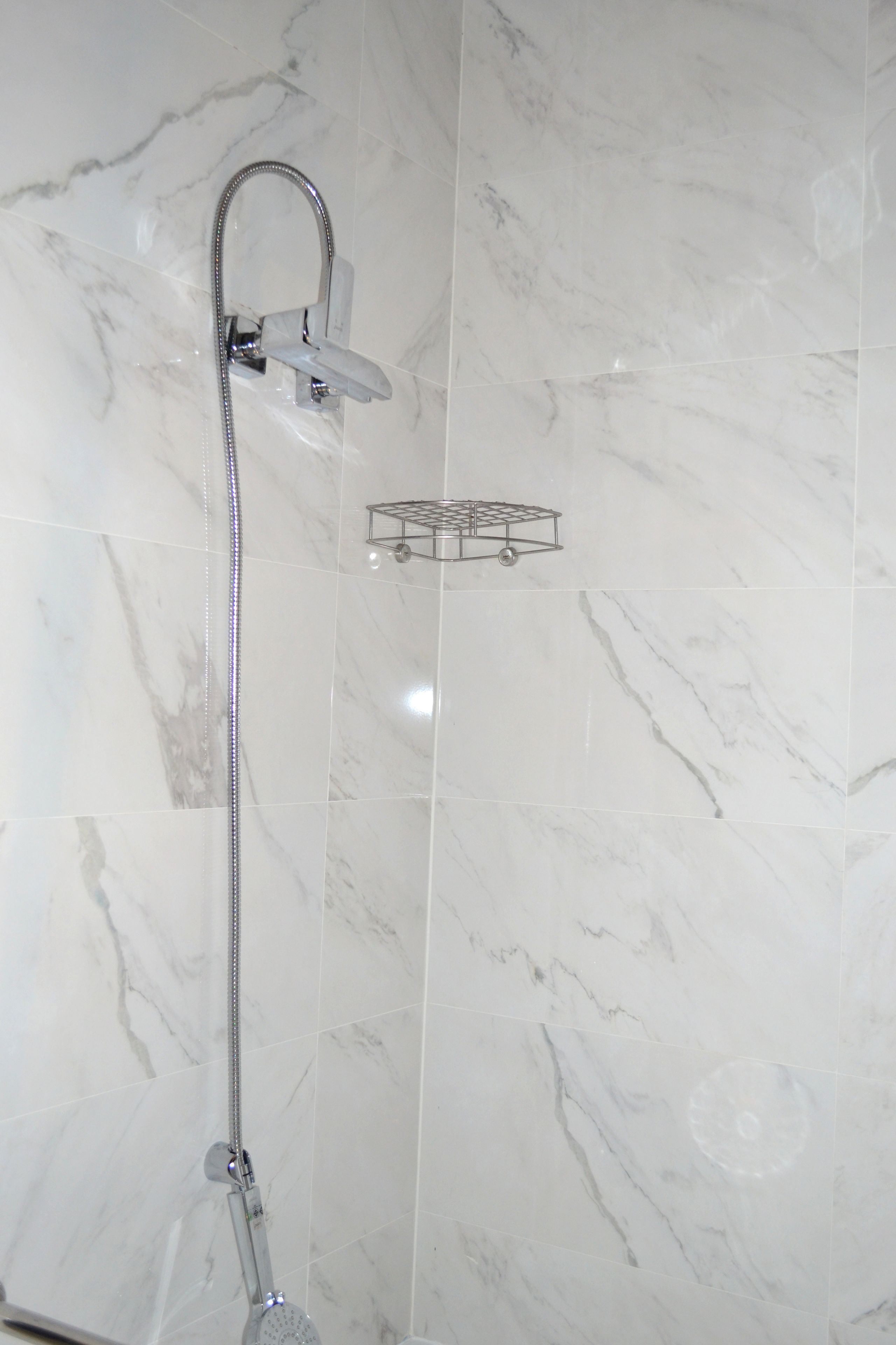 A shower with a handheld showerhead and a wall-mounted control panel.