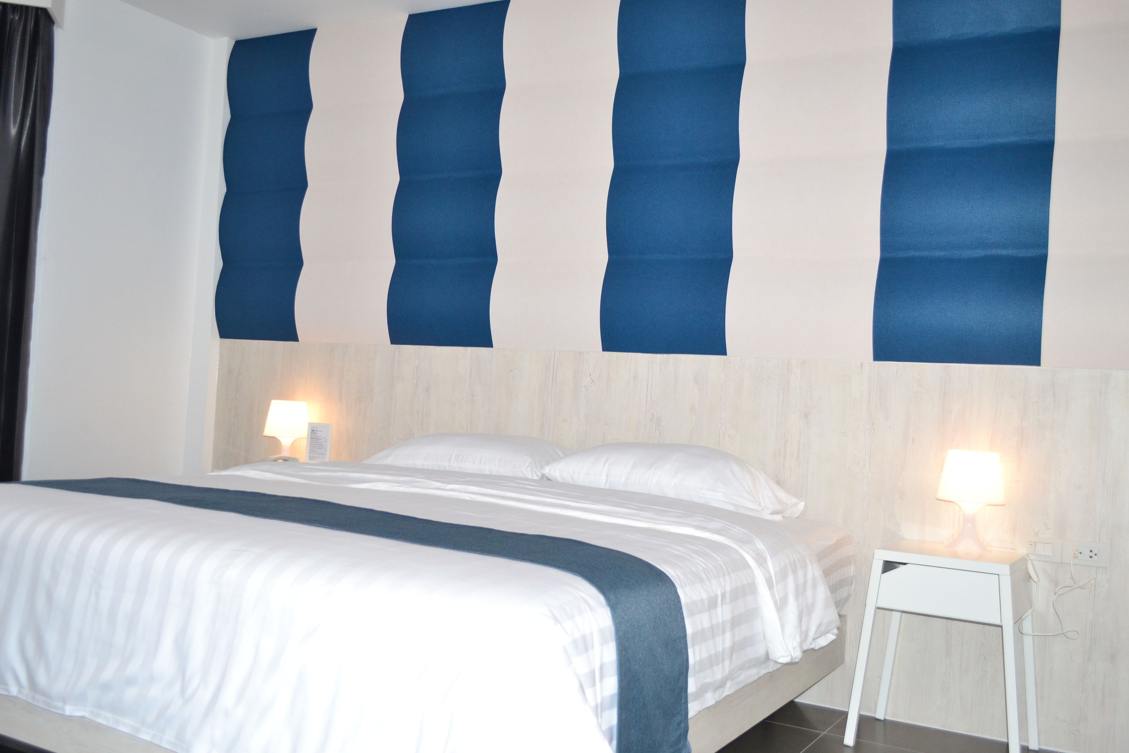 A hotel room with a bed, two bedside lamps, and a nightstand.