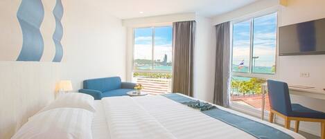 A hotel room with a large bed, a desk with a chair, a TV mounted on the wall, and a balcony with a view of the city.