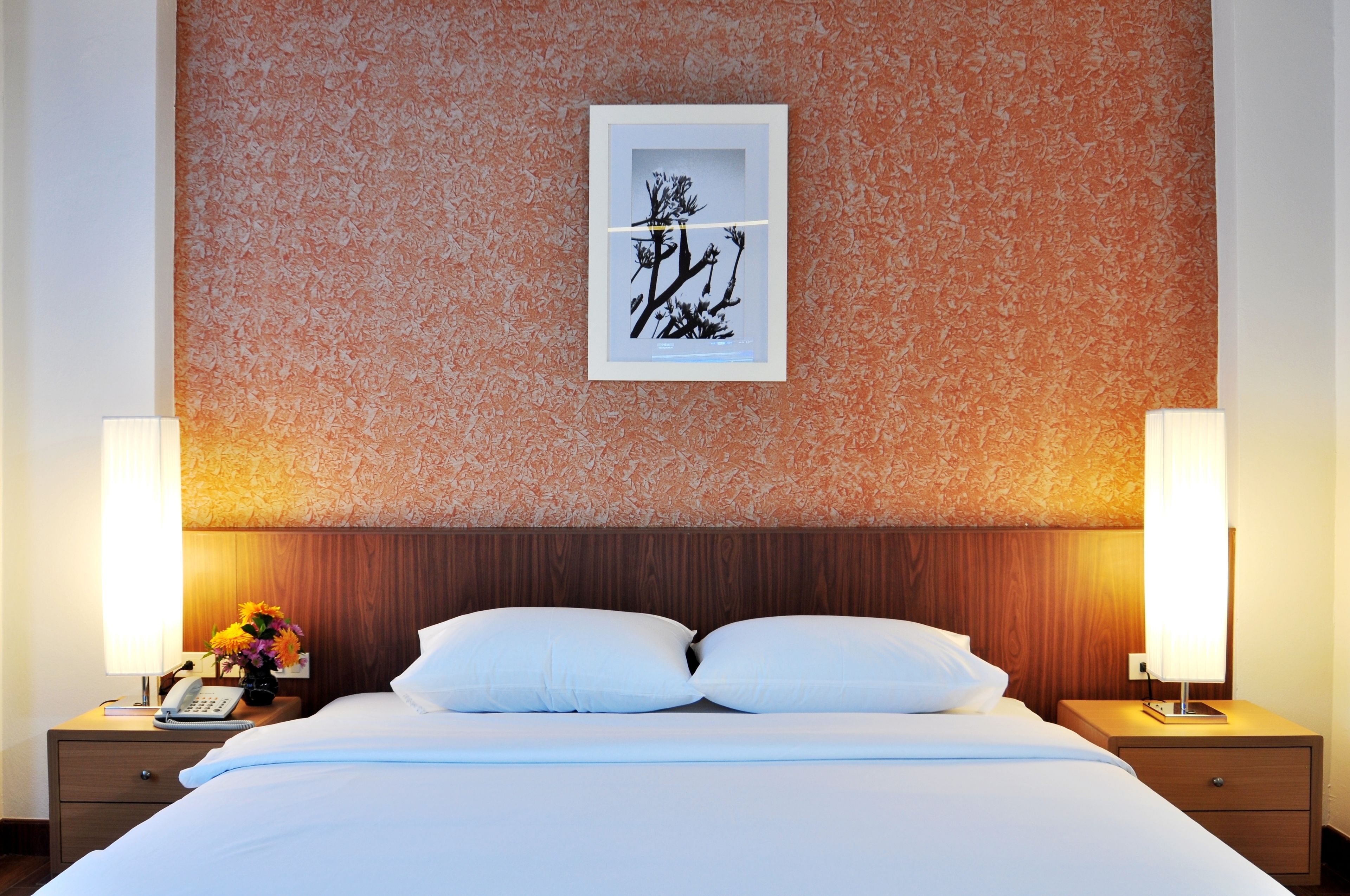 A hotel room with a bed, two bedside tables, a nightstand, a framed artwork, and a wall with a textured pattern.