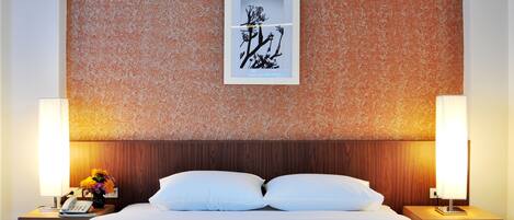 A hotel room with a bed, two bedside tables, a nightstand, a framed artwork, and a wall with a textured pattern.