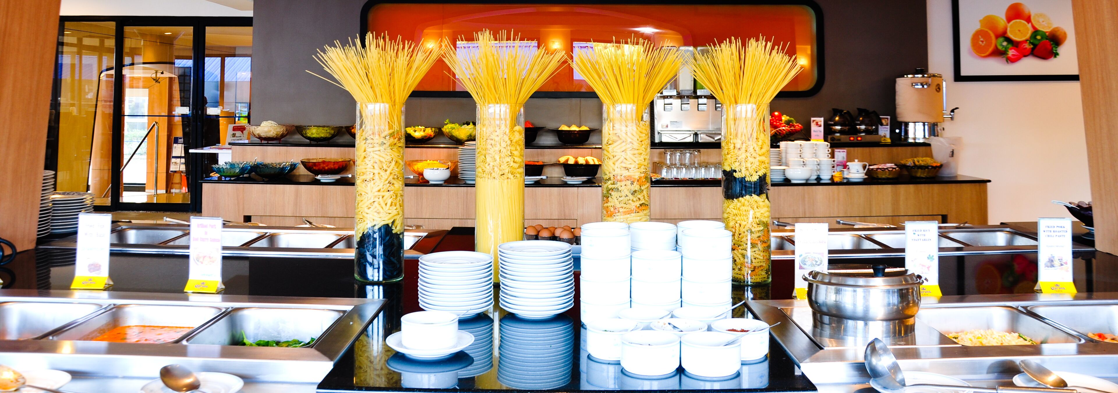 A buffet setup with pasta, plates, and bowls.