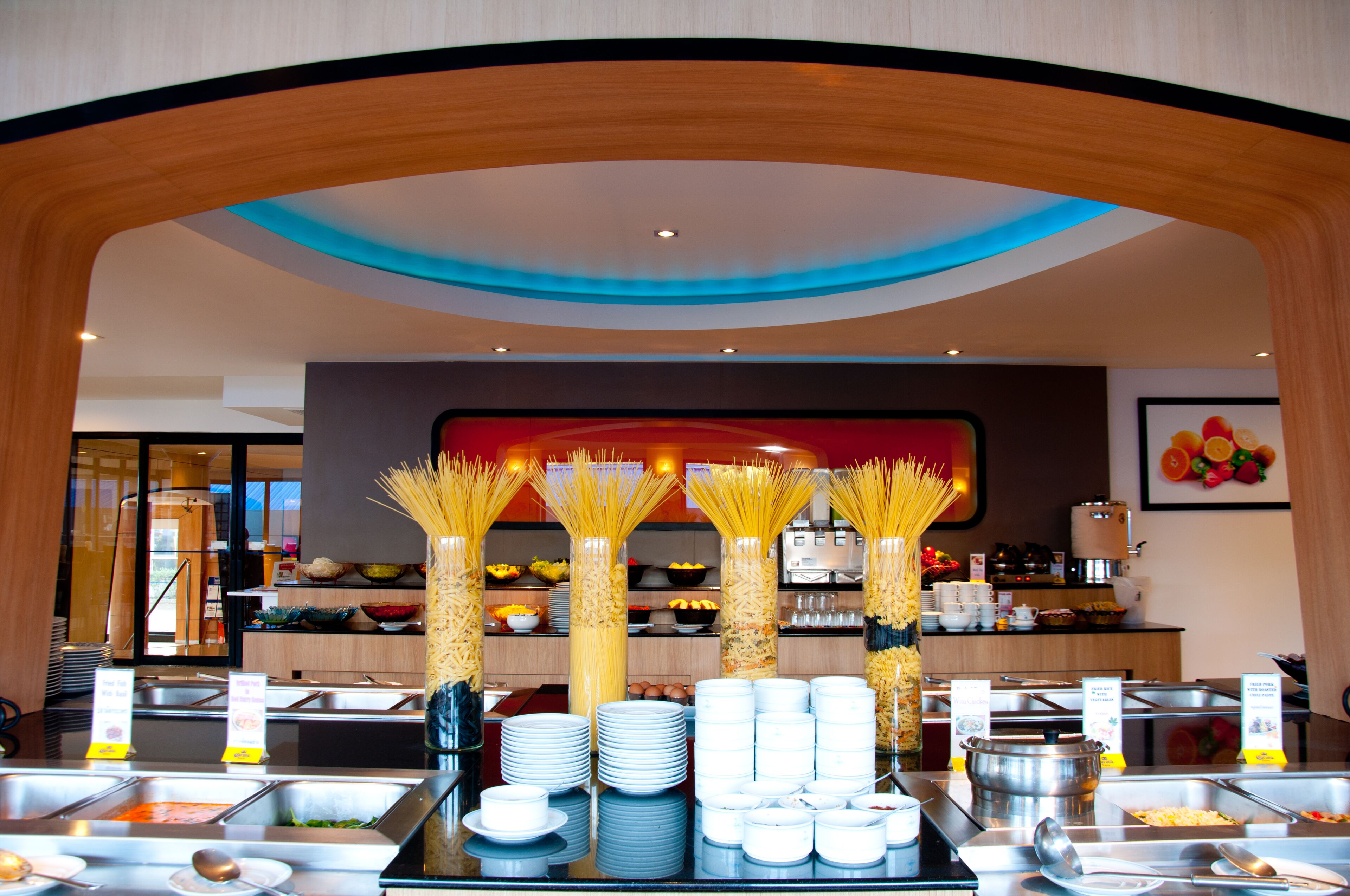 A buffet area with multiple food stations, a central display of stacked plates, and a decorative archway.