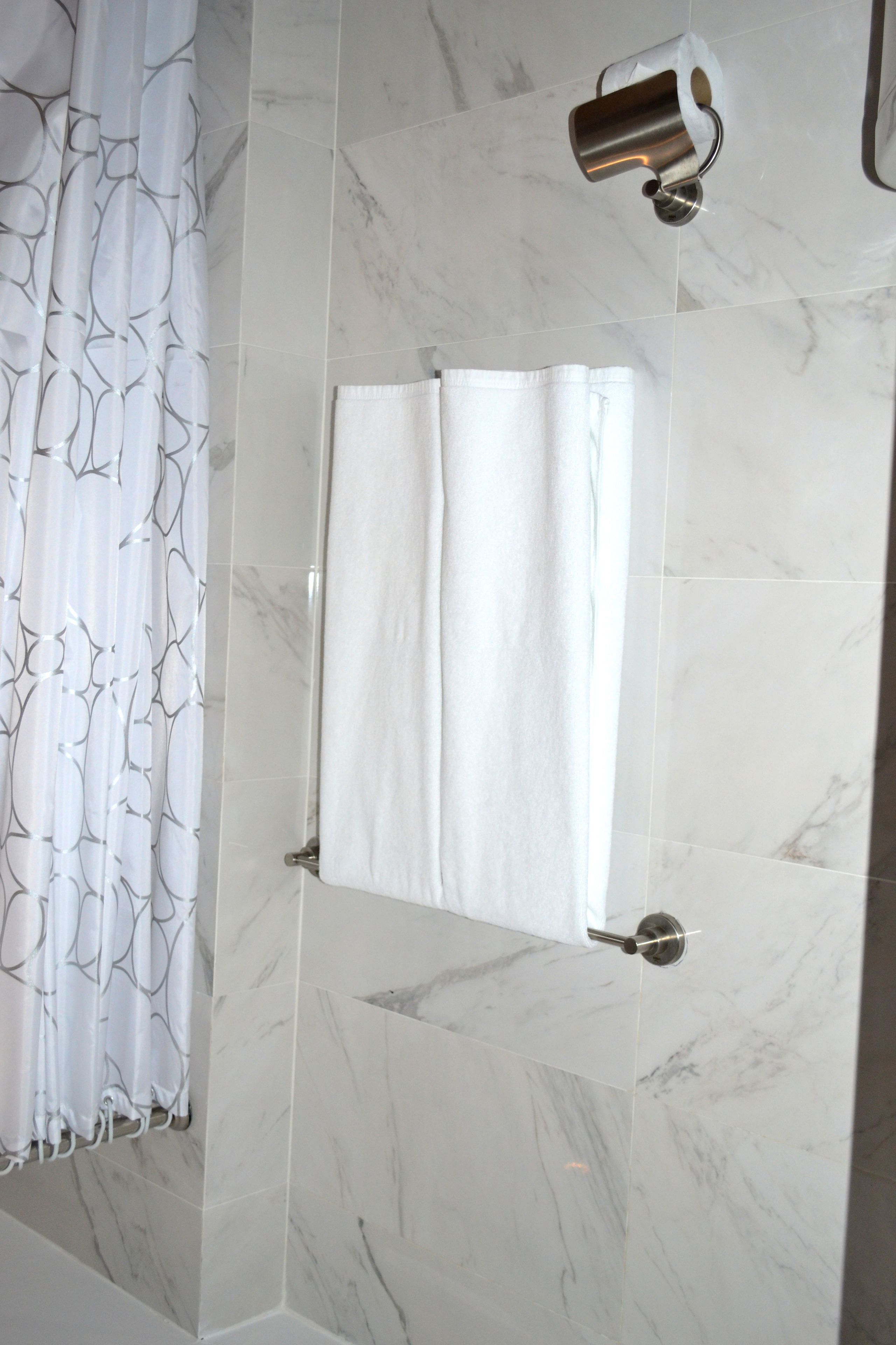 Un bany amb paret de marbre, penjador de tovalloles i cortina de dutxa.