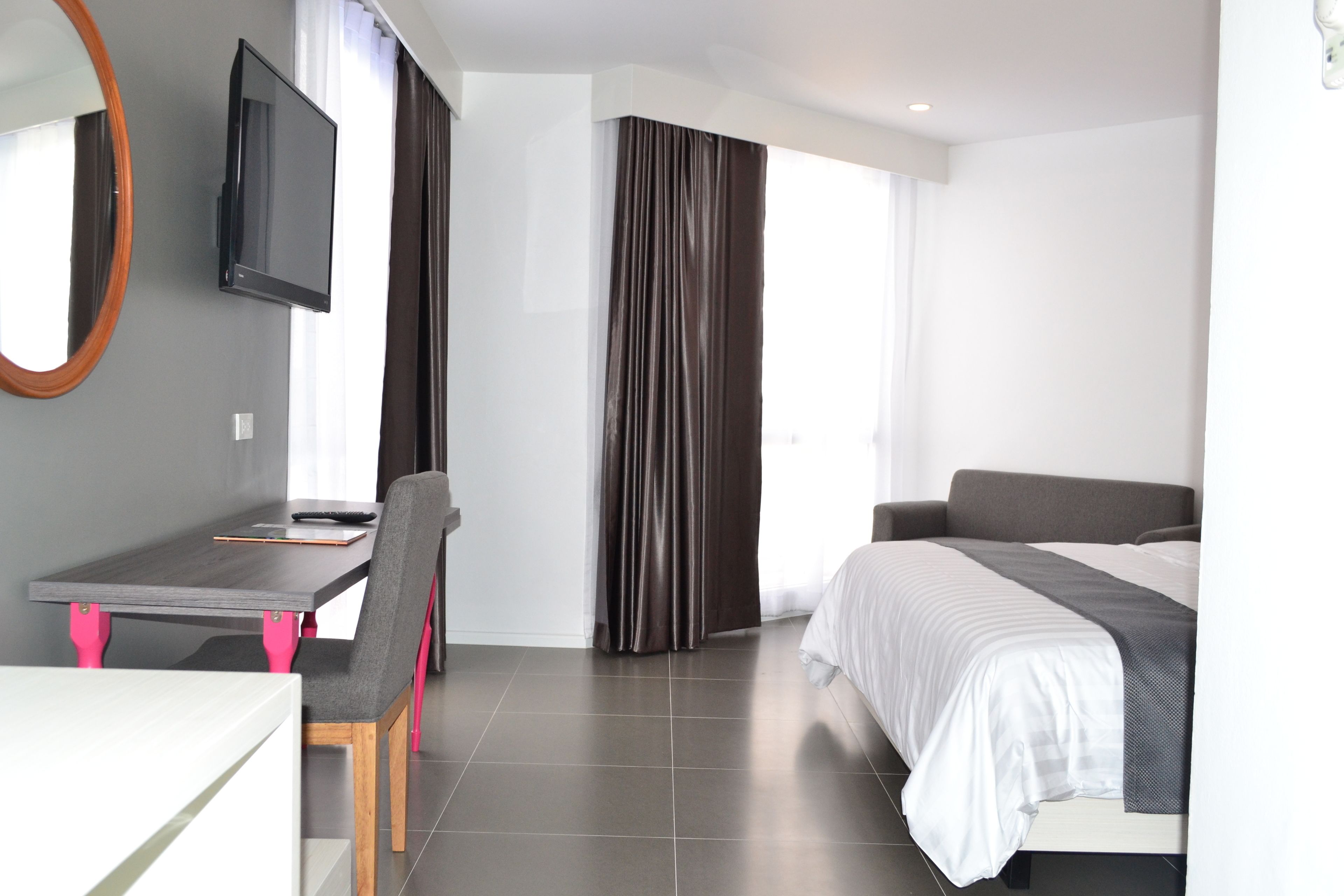 A modern hotel room with a bed, a desk, a chair, a TV, and a large window with curtains.