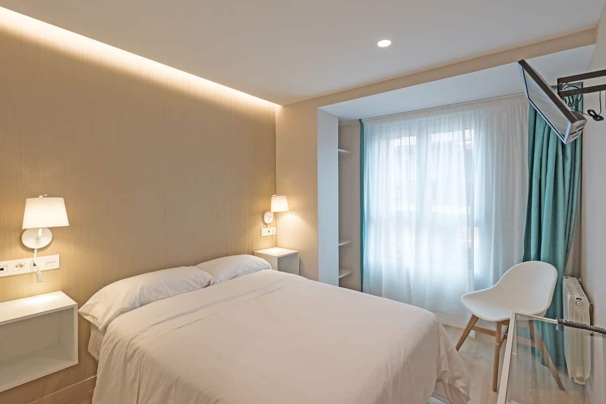 A modern hotel room with a large bed, bedside lamps, a glass table, and a chair.