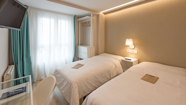 Ein Hotelzimmer mit zwei Betten, einem Schreibtisch, einem Fernseher und einem Fenster mit Vorhängen.