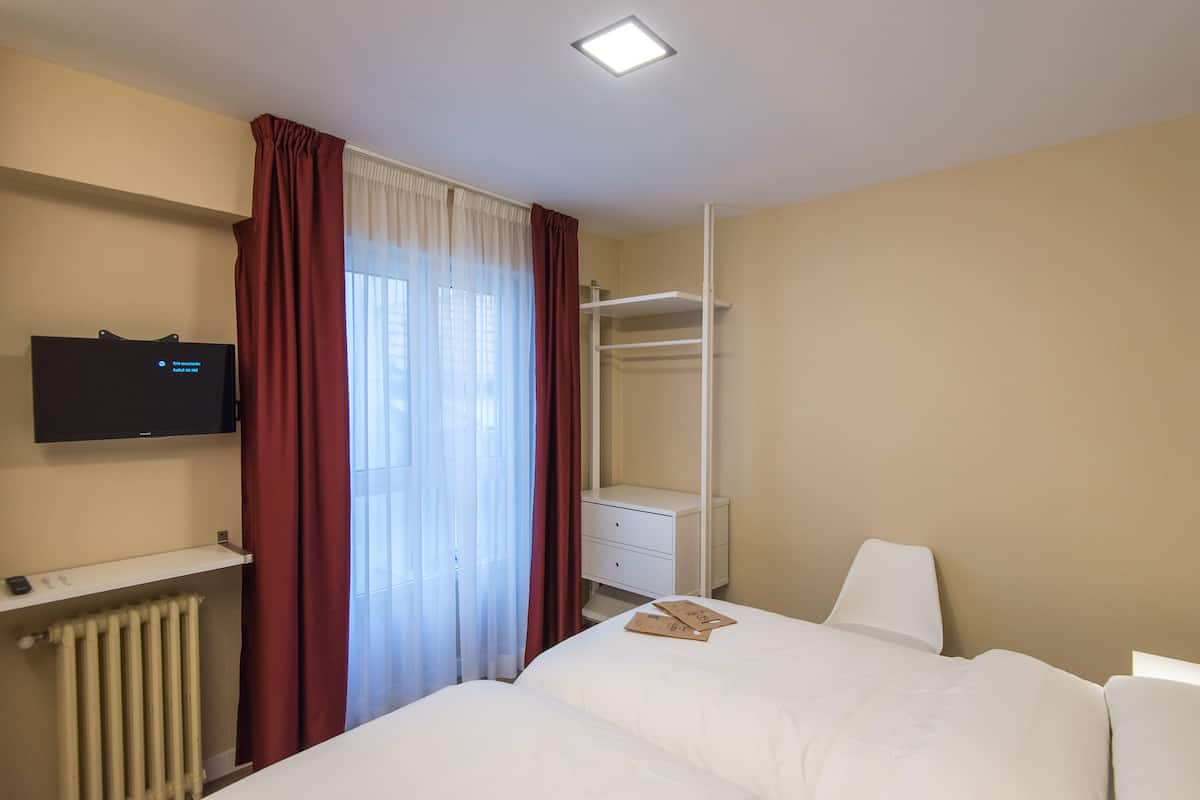 A hotel room with a bed, a TV mounted on the wall, a wardrobe, and a radiator.