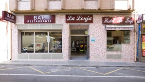Eine Bar und ein Restaurant namens 'La Lonja' mit einer gefliesten Fassade und Schildern, die auch eine Jugendherberge anbieten.