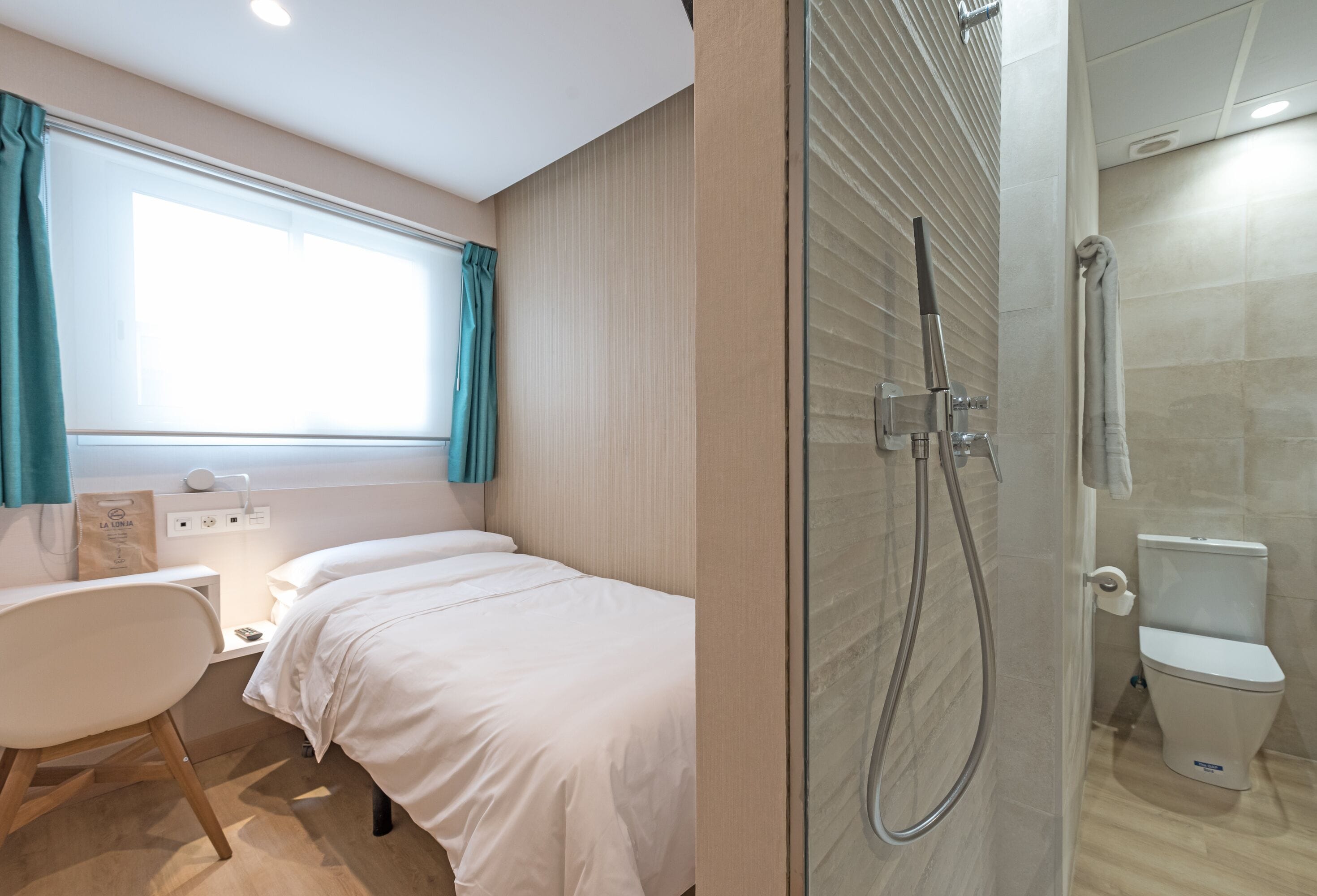 Hotelkamer met een bed, bureau, stoel, raam met gordijnen, douche en toilet.
