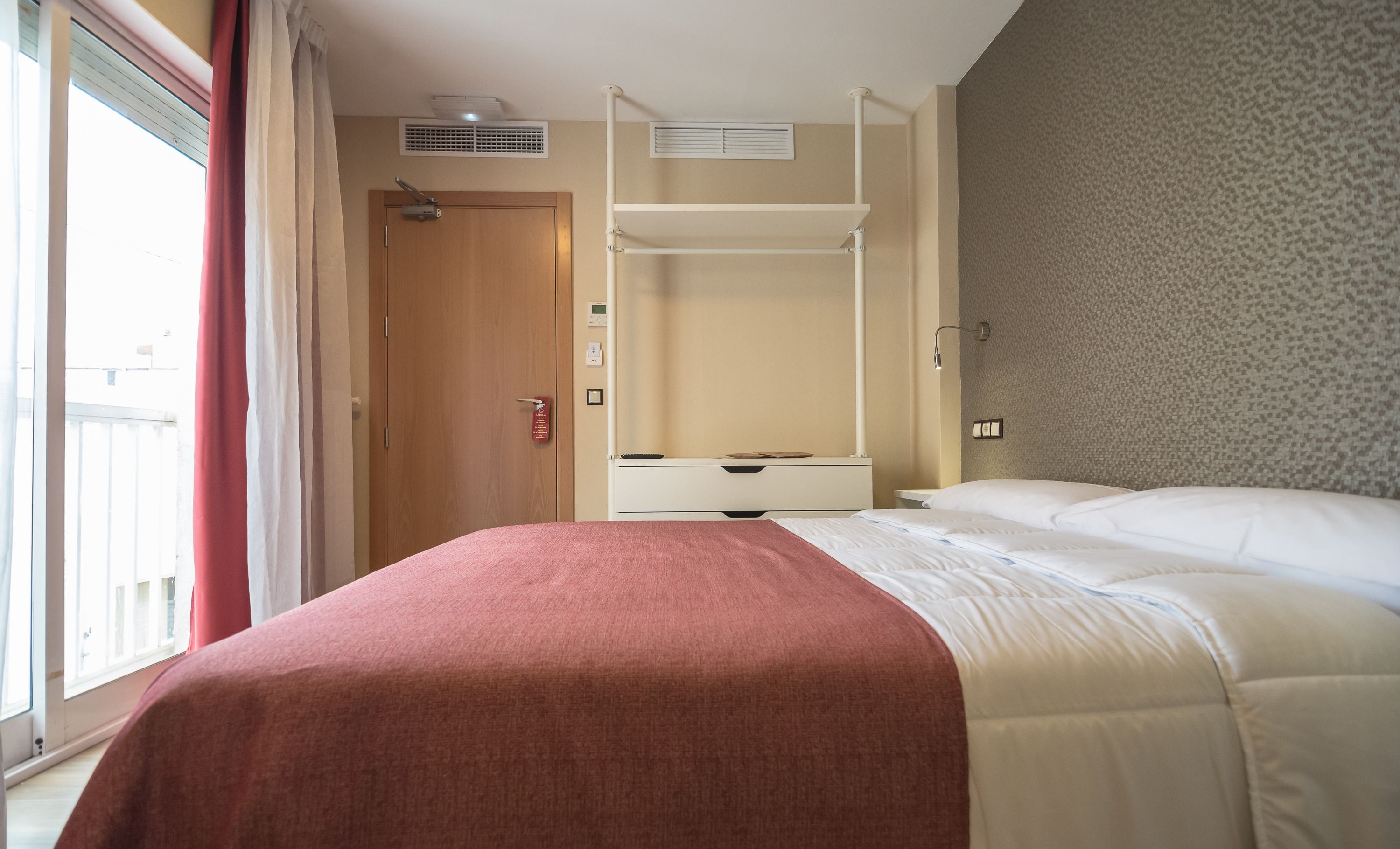 Una habitación de hotel con una cama, un armario, un escritorio y una ventana con cortinas.