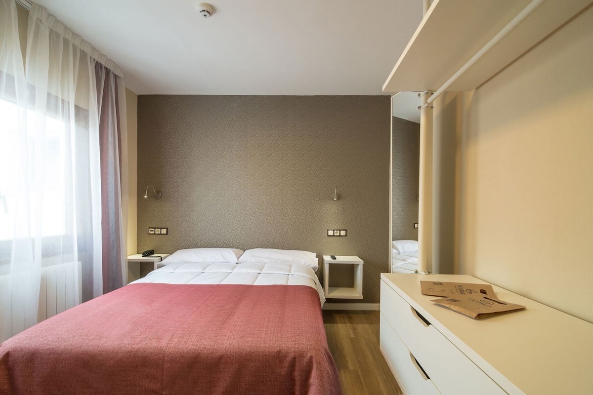 A hotel room with a bed, bedside tables, a mirror, and a dresser.