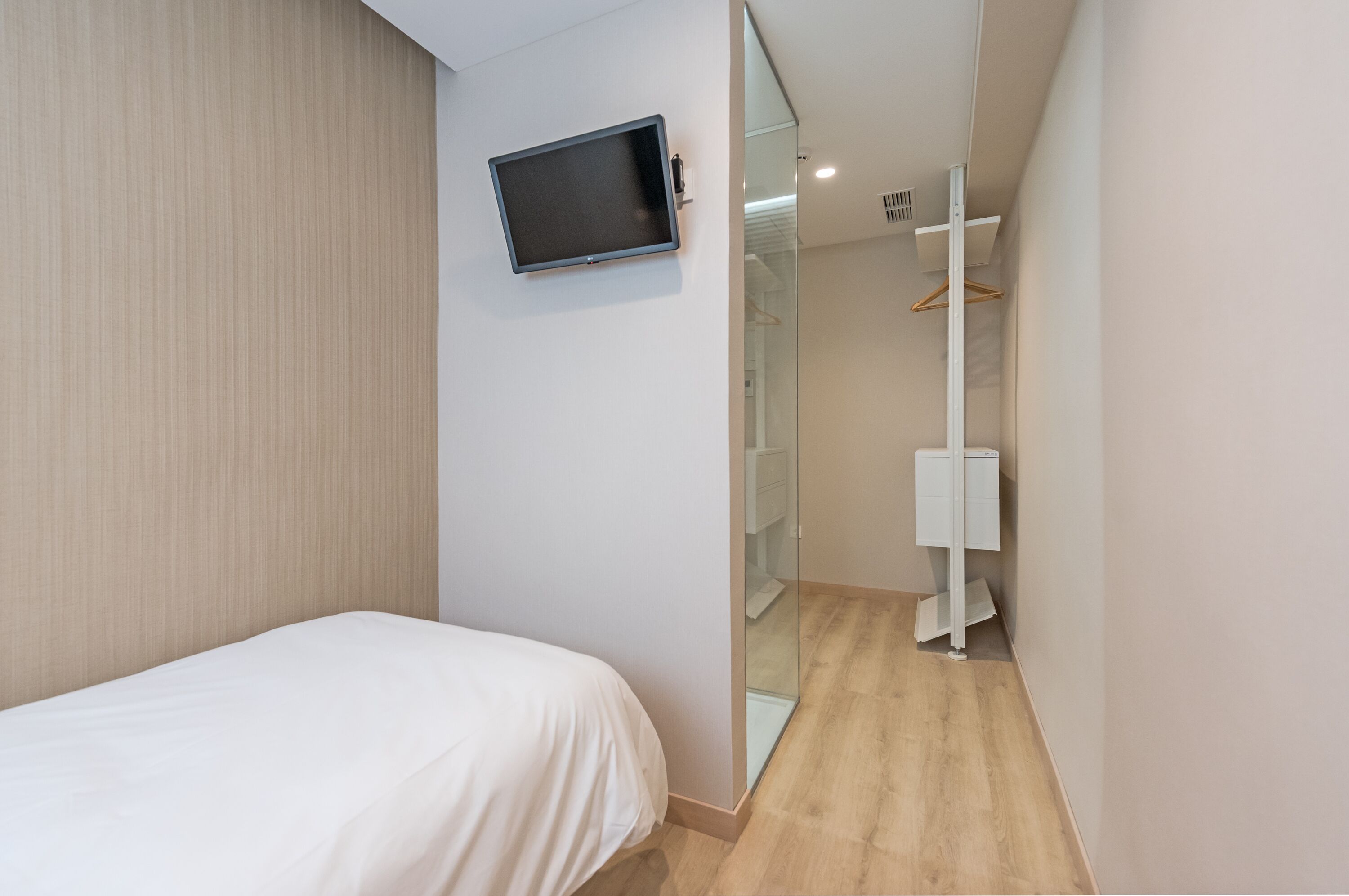 Una habitación de hotel moderna con una cama, un televisor en la pared, un vestidor y un espejo.