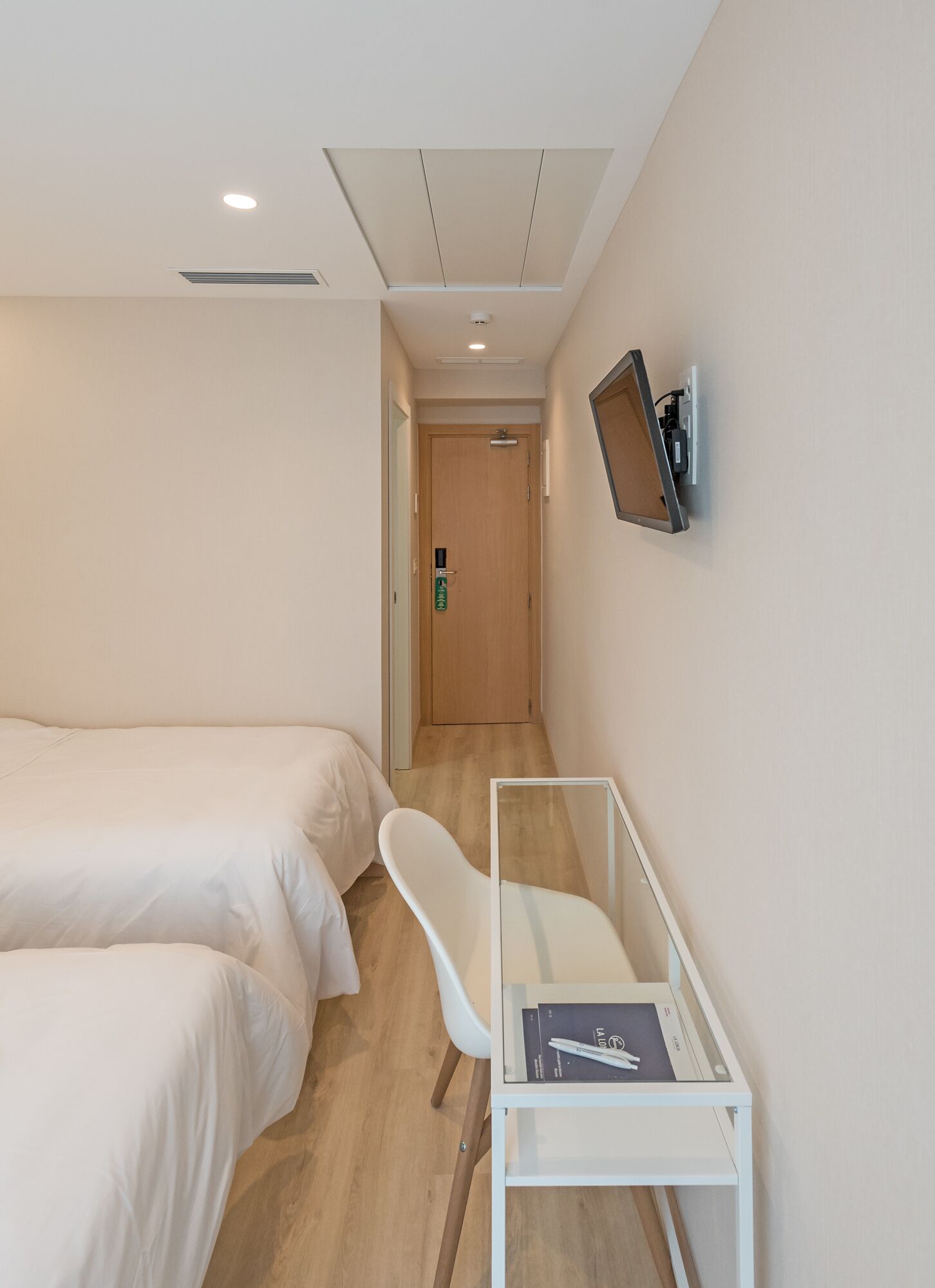 A hotel room with two beds, a desk with a printer, a chair, and a TV mounted on the wall.