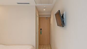 A hotel room with two beds, a desk with a printer, a chair, and a TV mounted on the wall.