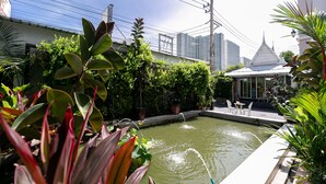 A courtyard with a small pond, potted plants, and a white building with a pointed roof. - Villa Lamai - Wong Amat House Pattaya (Pattaya)