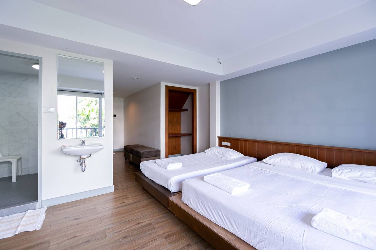 Ein Hotelzimmer mit zwei Betten, einem Holzkopfteil, einem großen Spiegel, einem Waschbecken und einem Holzboden.