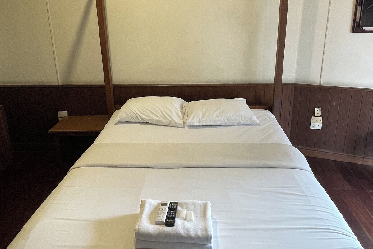 A single bed with a wooden frame, white bedding, and a remote control on the bed.