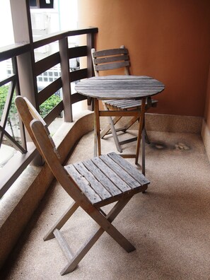 A balcony with a wooden table and chairs, a metal railing, and a view of the outdoors. - Keerati Homestay (Pattaya)