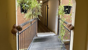A narrow hallway with a wooden floor, yellow walls, and an arched ceiling. There are potted plants hanging on the walls and a metal railing along the sides. - Keerati Homestay (Pattaya)