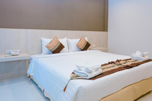 Una cama bien hecha con ropa de cama blanca y marrón, una mesita de noche con un teléfono, y una toalla doblada sobre la cama.
