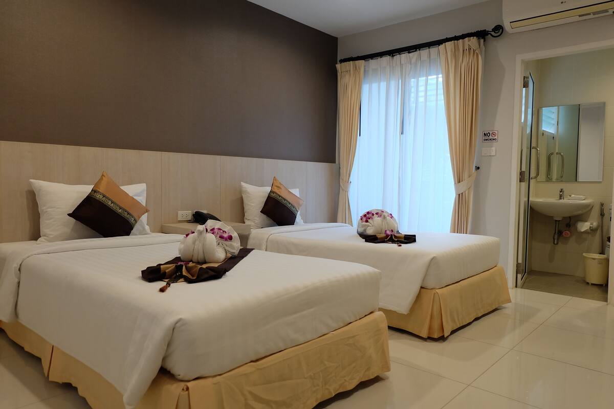 A hotel room with two beds, a bathroom, and a view of the outside.