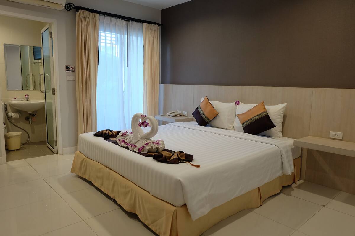 A hotel room with a bed, a bedside table, a nightstand, a bathroom with a sink, and a shower area.