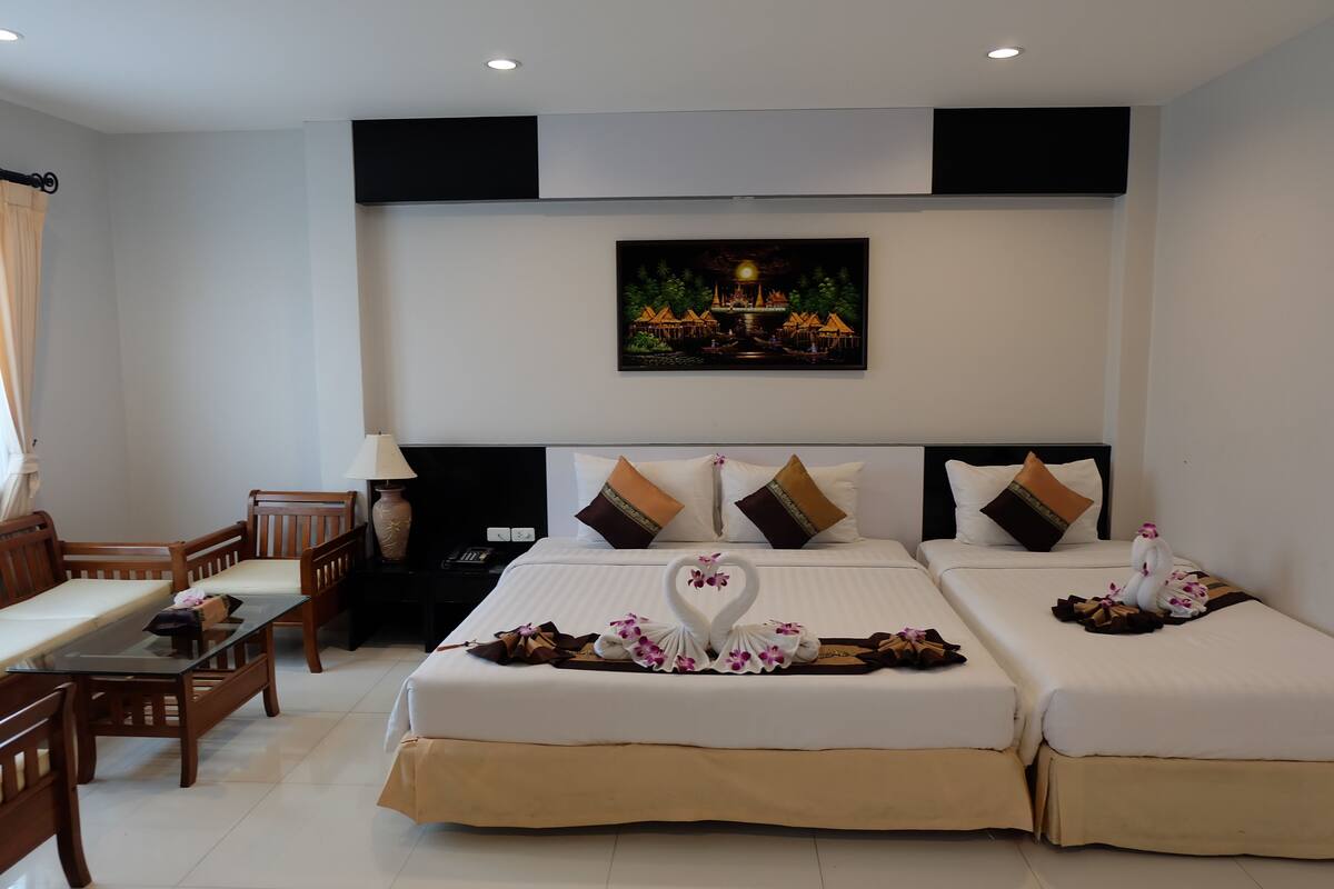 A hotel room with two beds, a dining table, chairs, and a painting on the wall.