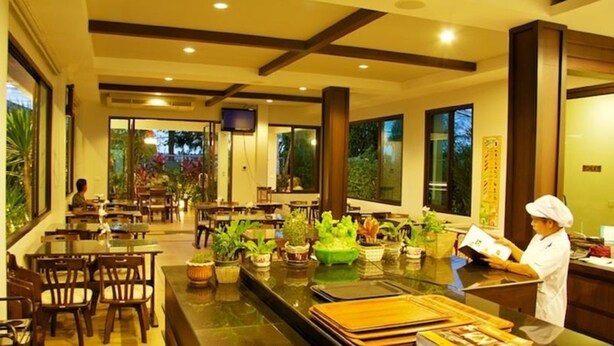 Un restaurant doté de nombreuses tables et chaises, d’un comptoir où travaille un chef, et de grandes fenêtres offrant une vue sur la verdure.