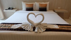 Une chambre d’hôtel avec un lit soigneusement fait, une décoration en forme de cœur faite avec des serviettes et un téléphone sur la table de chevet.