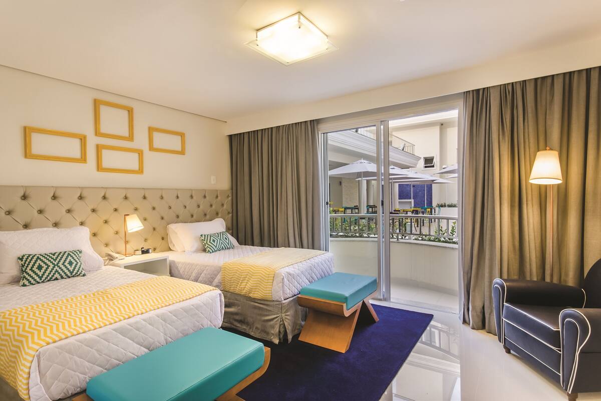 Une chambre d’hôtel avec deux lits, un canapé, un balcon avec vue et un bureau avec une lampe.