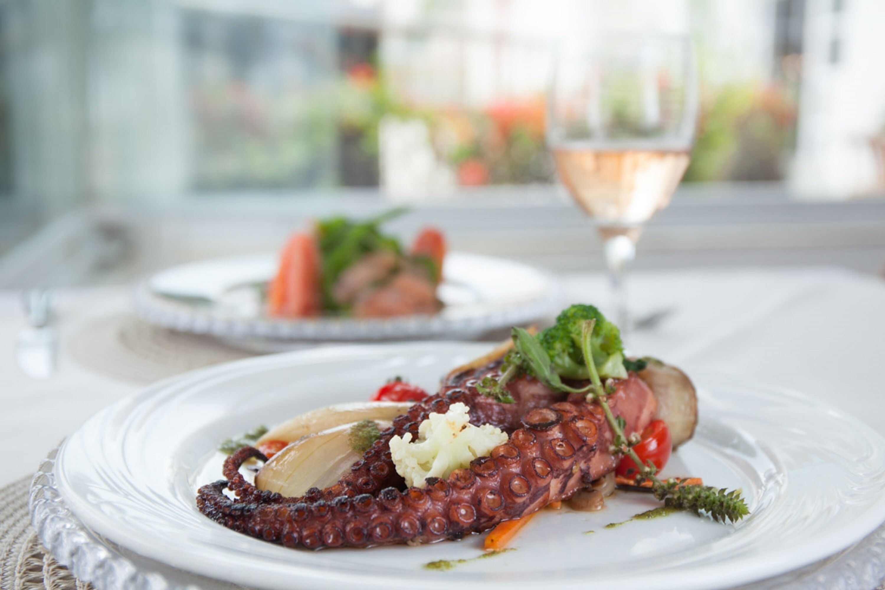 Prato de polvo com legumes e um copo de vinho sobre uma mesa.