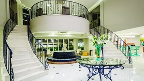 A spacious lobby with a central seating area, a glass-top table, and a spiral staircase with black railings. - Hotel Doral Guarujá (Guarujá)