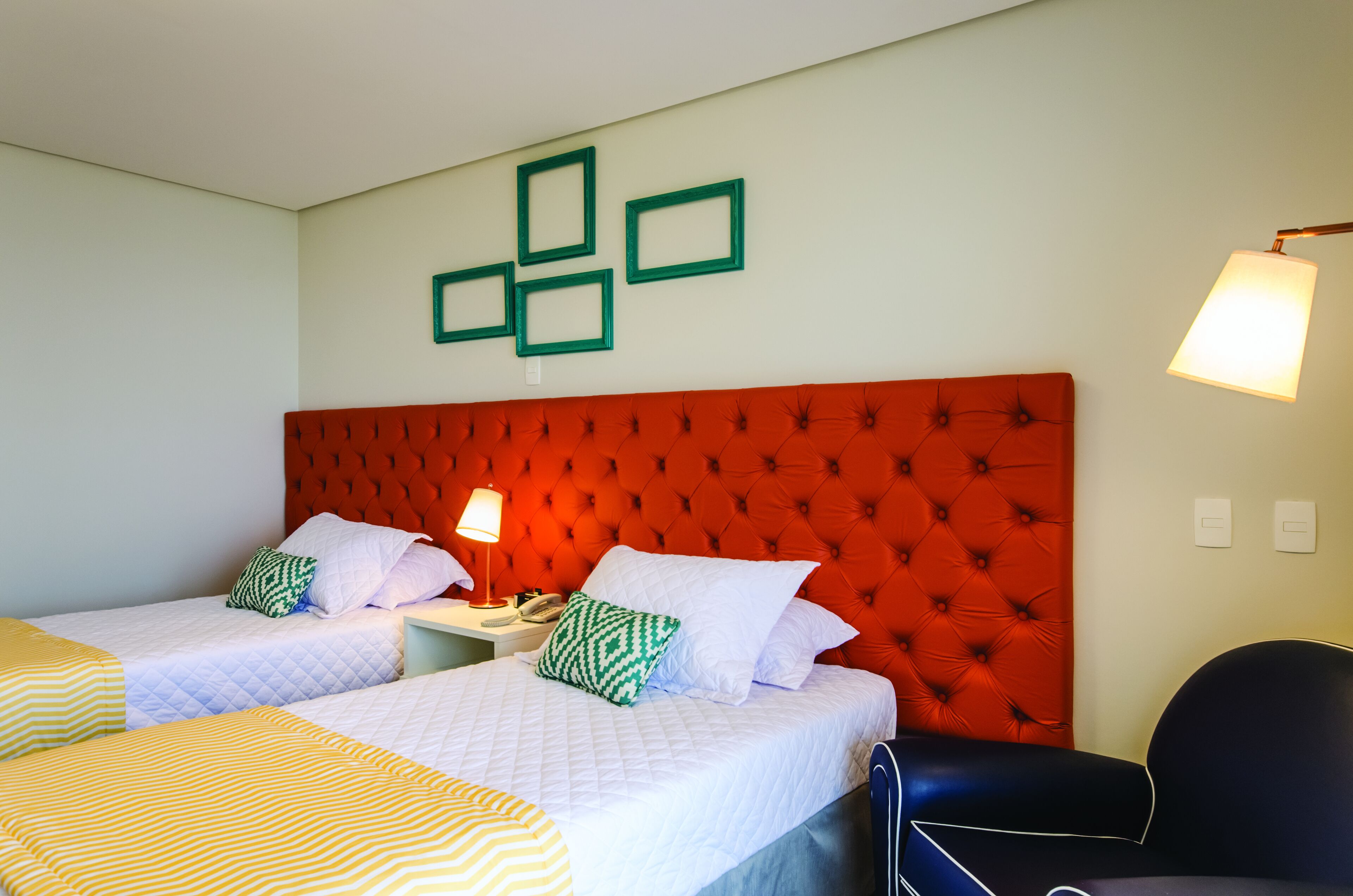 Habitación de hotel con dos camas, cabecero tapizado rojo, lámpara y una silla.