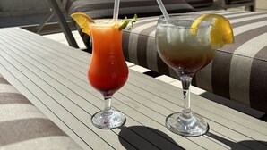 Two cocktails on a sunlit outdoor table with striped cushions and a canopy in the background. - Hotel Doral Guarujá (Guarujá)