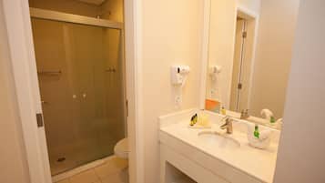 Un baño con ducha de vidrio, inodoro y lavamanos con espejo.