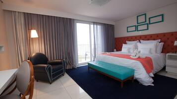 A hotel room with a bed, a desk, a chair, a window with curtains, and a wall with framed pictures.