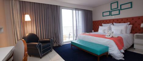 A hotel room with a bed, a desk, a chair, a window with curtains, and a wall with framed pictures.
