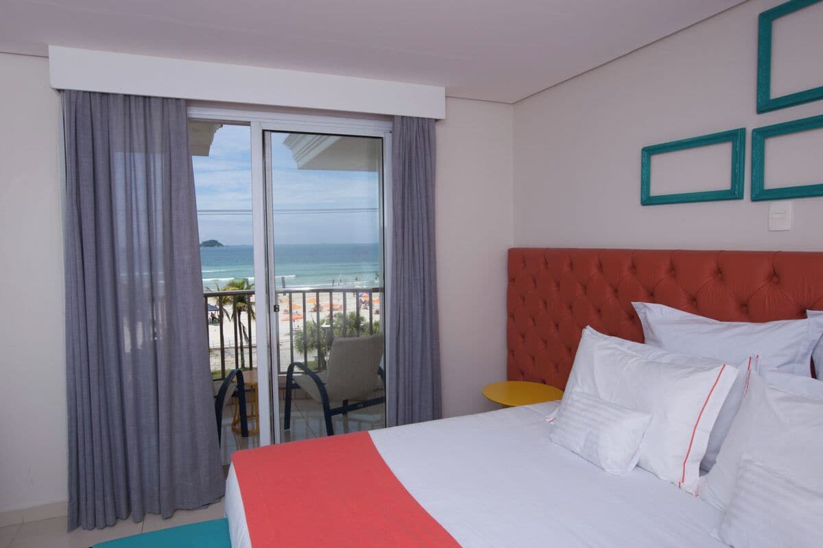A hotel room with a bed, a balcony with a view of the sea, and a red headboard.