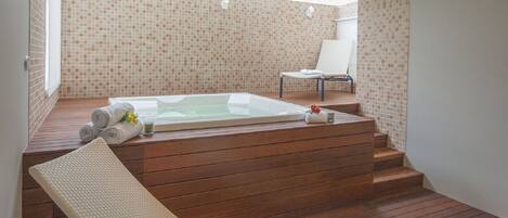 Un'area spa moderna con un solarium in legno, una vasca idromassaggio e una poltrona relax.