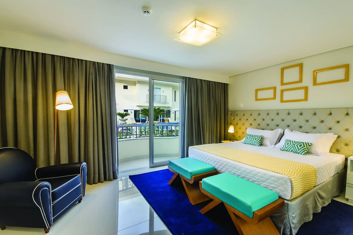 Une chambre d’hôtel avec un grand lit, un canapé, un banc et une vue sur le balcon extérieur.