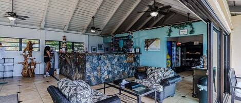 Un hall d’entrée spacieux avec un plafond haut, un espace salon central agrémenté de canapés à motifs, un coin bar avec un mur bleu et un escalier menant à un niveau supérieur.
