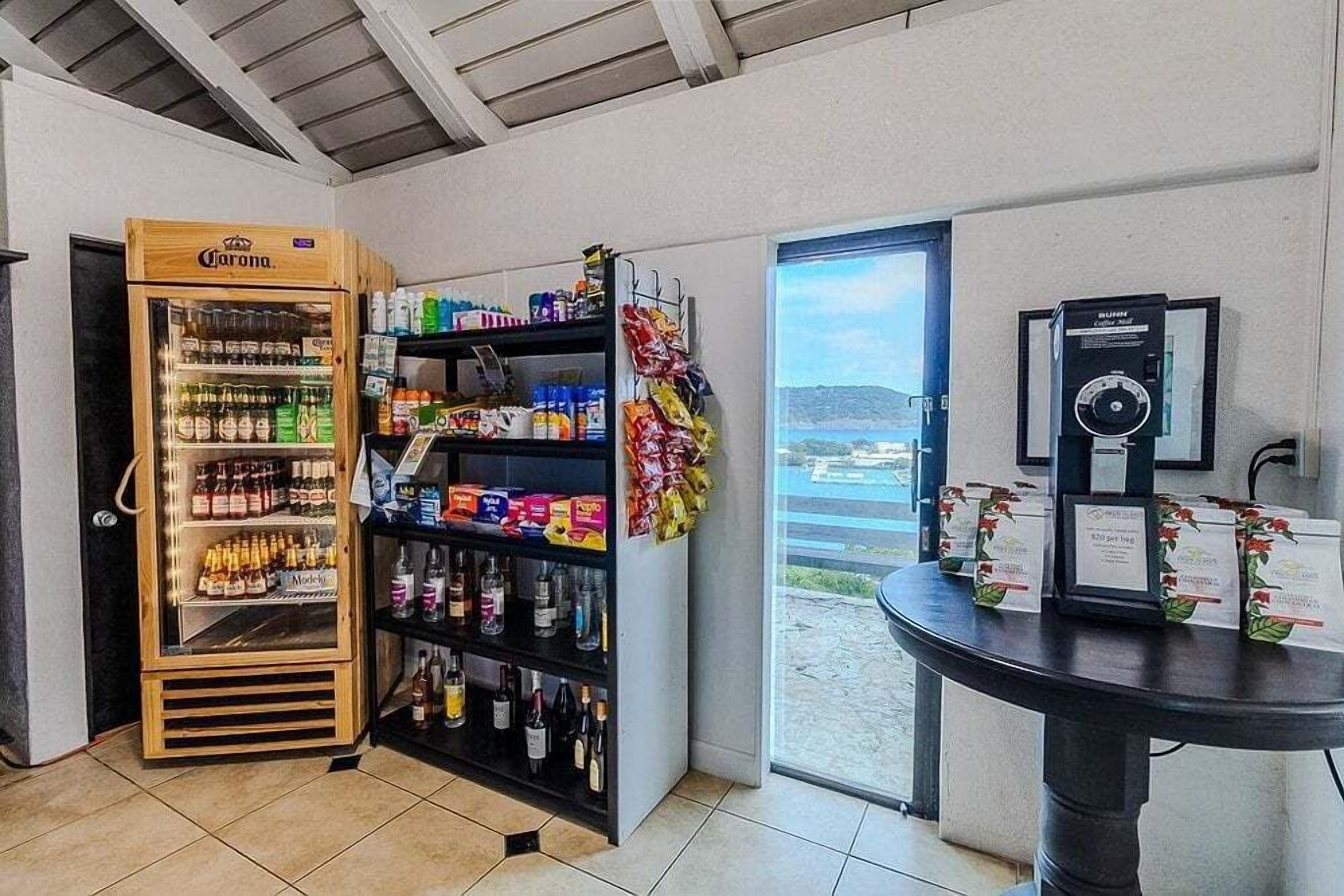 A room with a minibar, shelves stocked with snacks, a door leading outside, and a table with a coffee machine.