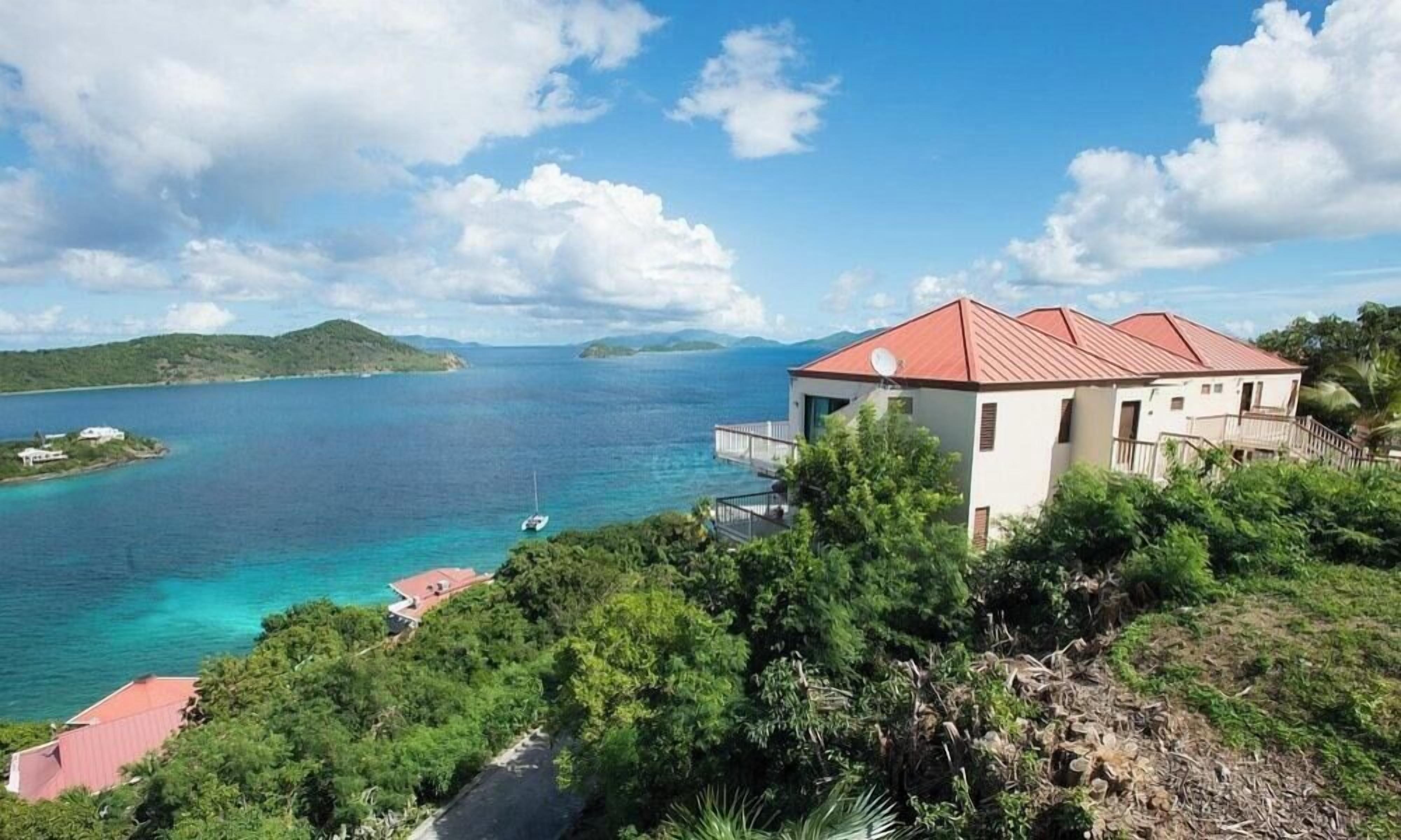 A coastal property with a red-roofed building, a clear view of the sea, and lush greenery.