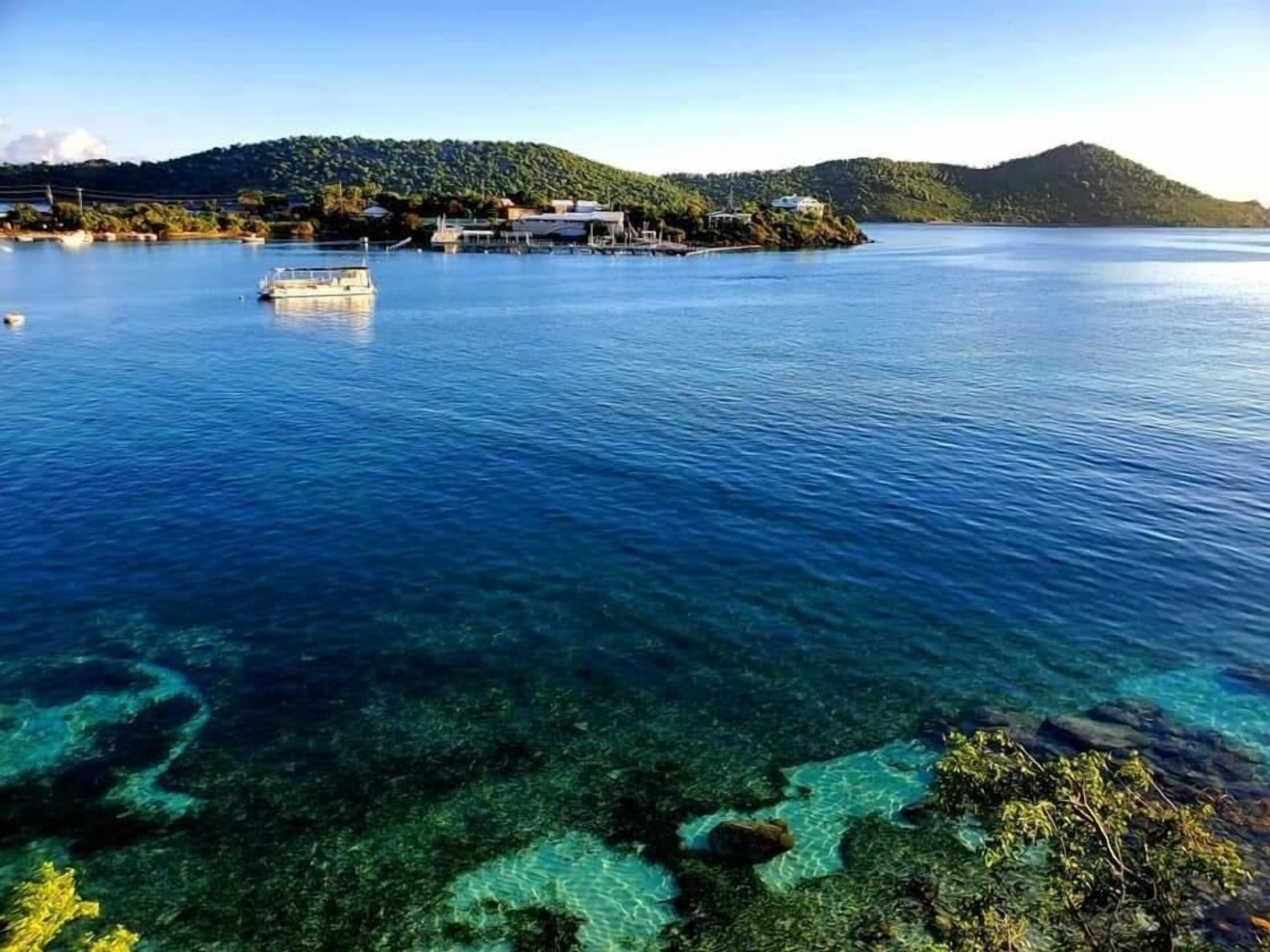 A coastal area with clear waters, a boat, and a small island with buildings.