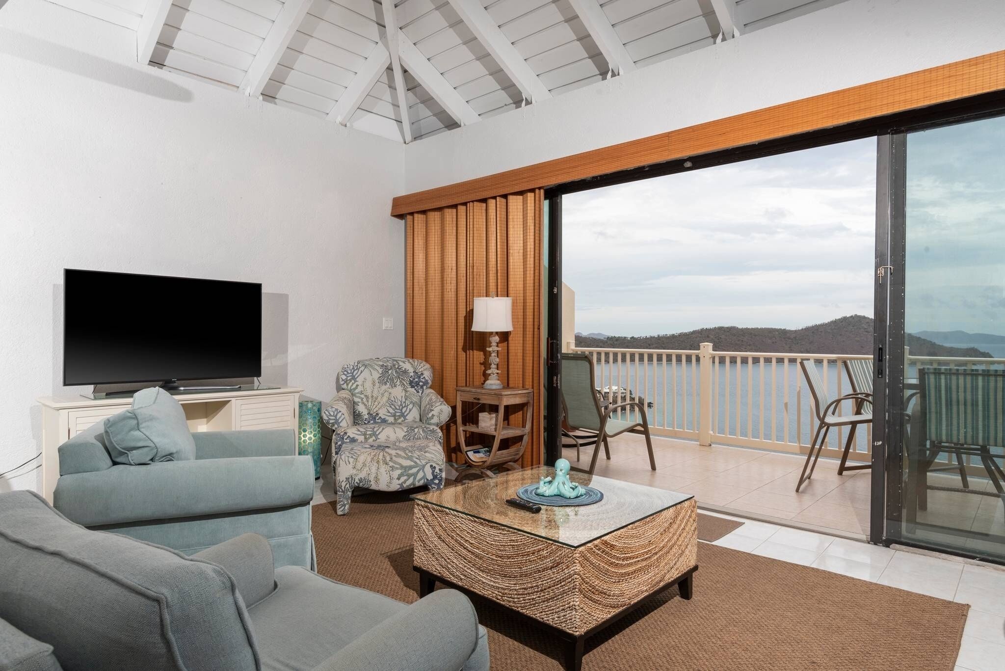 Een moderne woonkamer met een flatscreen-televisie, een bank, een gestreept fauteuil, een salontafel en een balkon met uitzicht op de bergen.