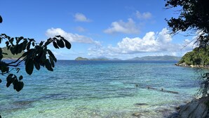 A beach with clear water, rocky shore, and distant islands. - Point Pleasant Resort (St. Thomas)