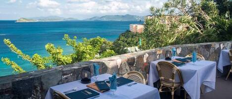 A seaside restaurant with tables set for dining, overlooking the ocean.