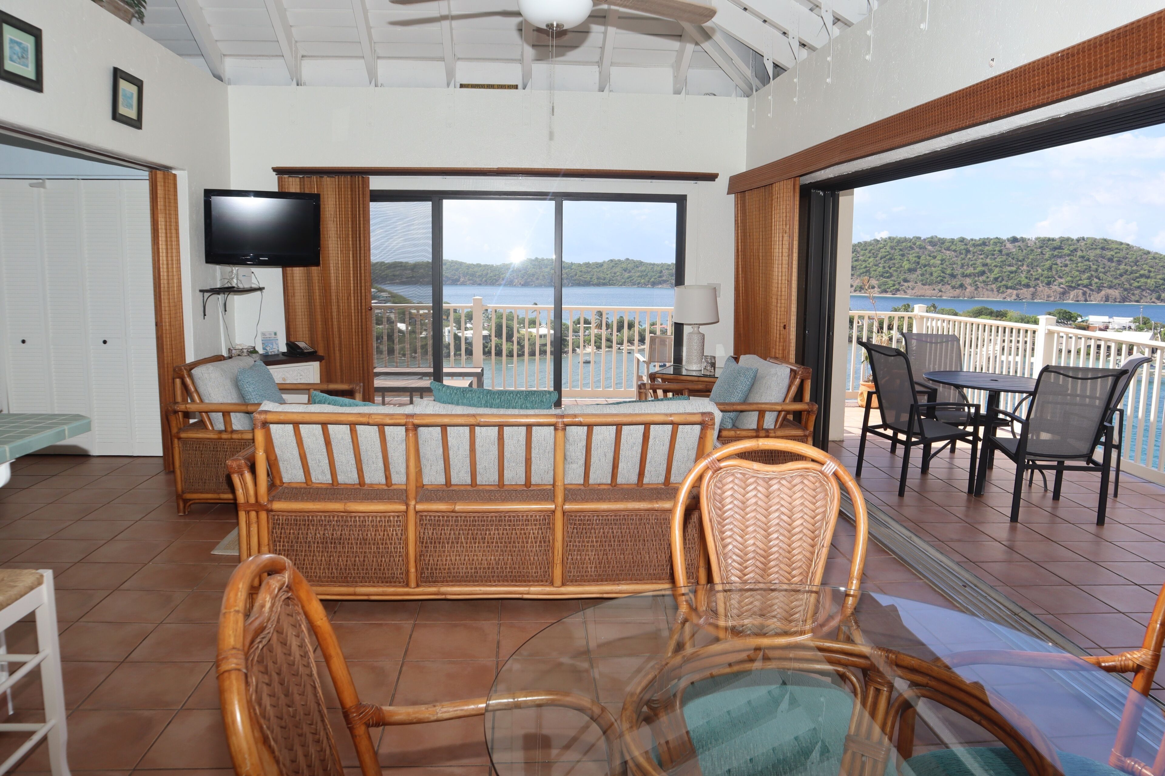 A room with a balcony, a television, wicker furniture, and a view of a body of water.