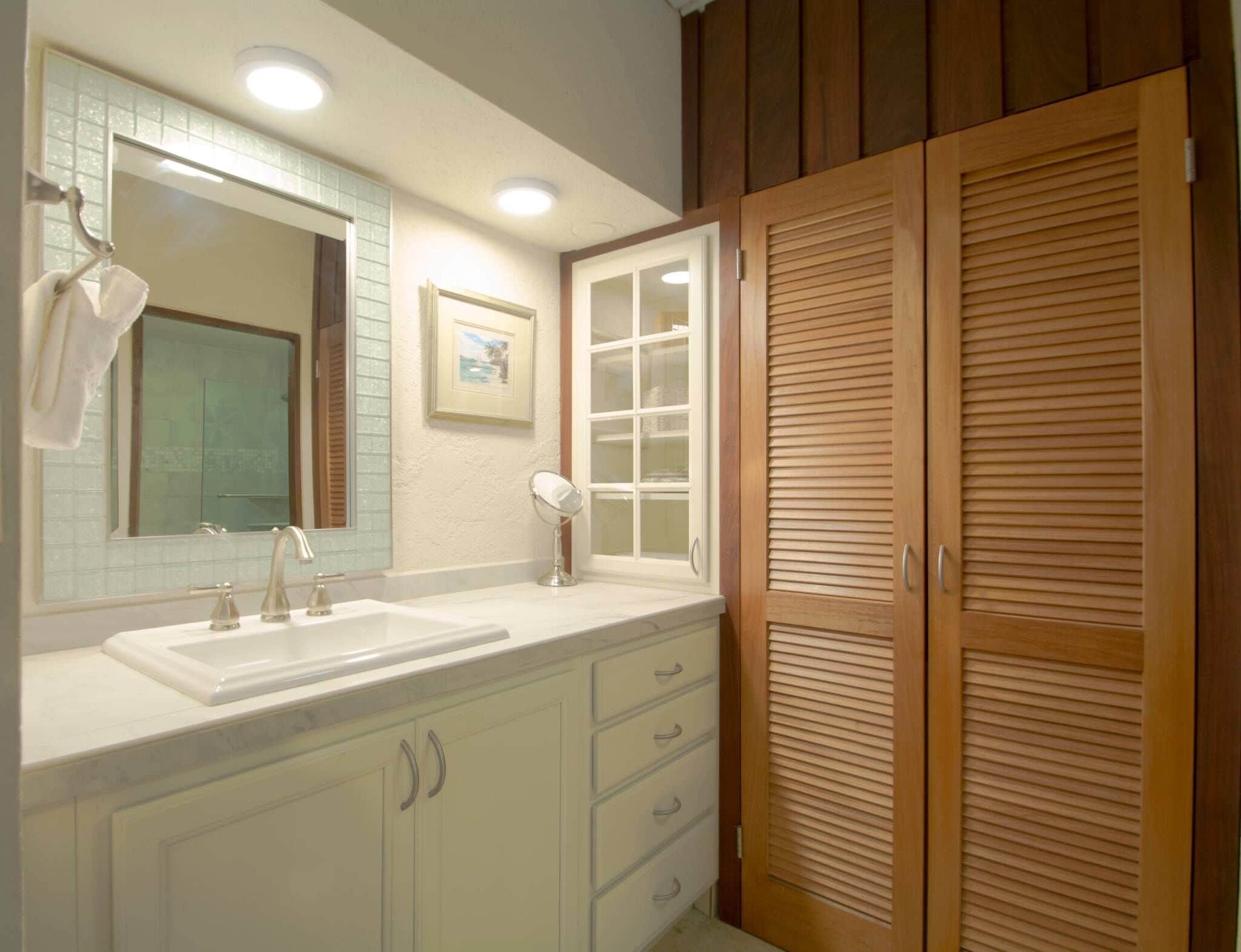 A bathroom with a white vanity, a large mirror, a framed picture on the wall, and wooden cabinets.